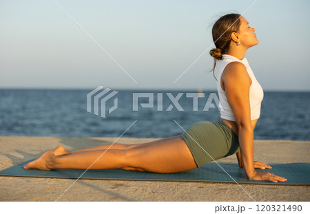 Young girl practicing bhujangasana yoga pose on mat on seashore 120321490