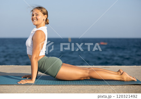 Flexible girl practicing cobra pose of yoga on seashore 120321492