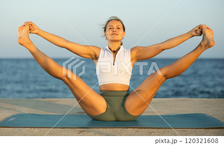 Girl practicing hatha yoga on sea beach, stretching in an asymmetrical seated asana Parivritta Janu Sirsasana Girl practicing hatha yoga on sea beach, stretching in an asymmetrical seated asana Parivritta Janu Sirsasana 120321608