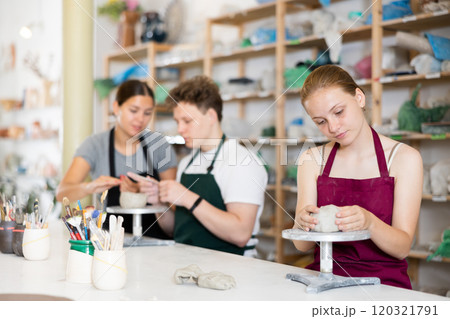Young woman teacher helps teenagers boy and girl to sculpt ceramic product Young woman teacher helps teenagers boy and girl to sculpt ceramic product 120321791