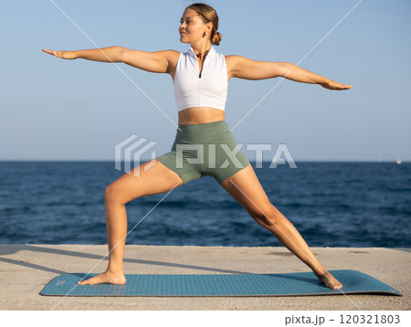 Sportive girl practicing warrior pose of yoga on seashore Sportive girl practicing warrior pose of yoga on seashore 120321803