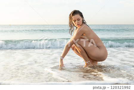 Young nude woman posing sitting on beach 120321992
