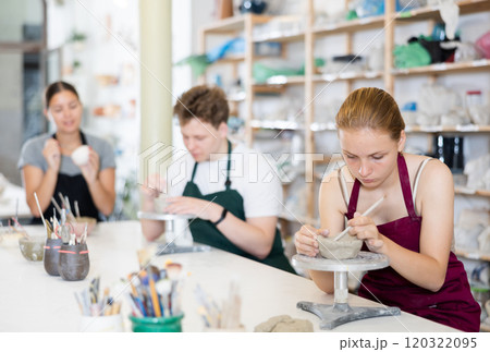 Teenage girl attentively learns how to make pottery with a wooden sticker in workshop 120322095