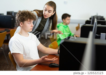 Female teacher consulting concentrated teenager in computer class 120322123