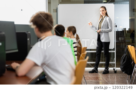 Teacher standing at marker board in computer class in front of pupils Teacher standing at marker board in computer class in front of pupils 120322149