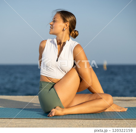 Flexible girl practicing lord of the fishes pose of yoga on seashore 120322159