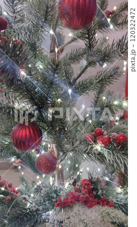A close-up of a Christmas tree adorned with red ornaments and white lights. The tree is covered in a light dusting of artificial snow, creating a festive and magical atmosphere 120322472