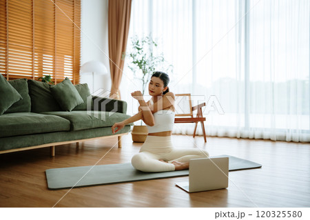 Happy young Asian woman practicing yoga and shoulder stretching at home Happy young Asian woman practicing yoga and shoulder stretching at home 120325580