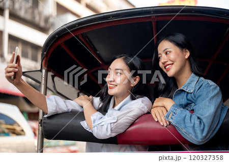 Two happy Asian girls take a selfie together while exploring the city and enjoying a tuk-tuk ride. Two happy Asian girls take a selfie together while exploring the city and enjoying a tuk-tuk ride. 120327358