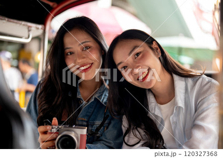 Two happy, charming young Asian girls enjoy a ride in a tuk-tuk in Thailand, smiling at the camera. 120327368