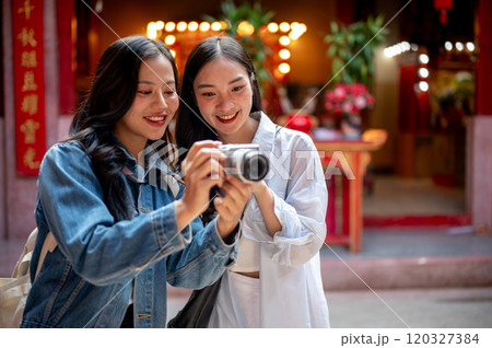 Two happy, pretty Asian female friends visit a Chinese shrine, checking photos on a camera together. Two happy, pretty Asian female friends visit a Chinese shrine, checking photos on a camera together. 120327384