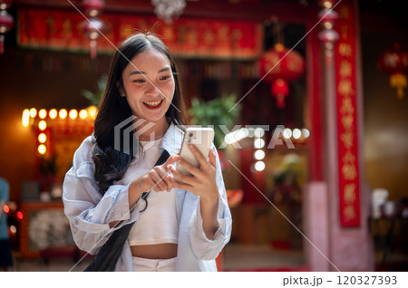 A smiling Asian female tourist using her smartphone while visiting a stunning Chinese shrine. 120327393