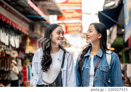 Two happy Asian female tourists explore a local market in Thailand, walking along the street. Two happy Asian female tourists explore a local market in Thailand, walking along the street. 120327415
