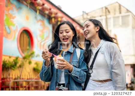 Two joyful Asian female friends explore the city in Chiang Mai, Thailand, enjoying ice cream. Two joyful Asian female friends explore the city in Chiang Mai, Thailand, enjoying ice cream. 120327427