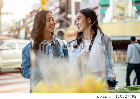 Two cheerful, cute Asian female tourists buy street food in Thailand. 120327492