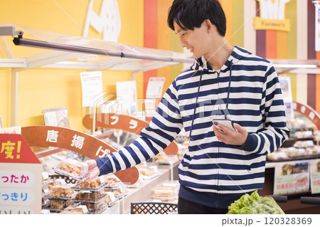 スマホを片手にスーパーで買い物をする若い男性 120328369