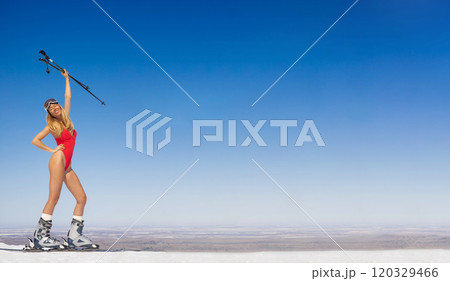 Attractive happy woman model in red swimsuit with skis on ski slope. 120329466