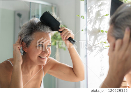 European beautiful and smiling middle-aged woman combing her gray hair European beautiful and smiling middle-aged woman combing her gray hair 120329533