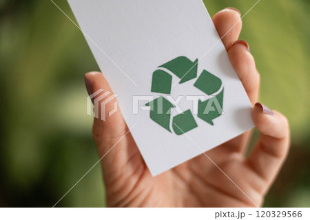 Hand takes a label with a recycling icon. Recyclable product concept. Green background of plants. 120329566