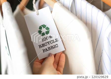 Female hands hold a label from white knitted clothing, on which it says 100 percent recycle fabric 120329629