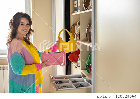 A happy, smiling, beautiful woman chooses a fashionable bag for herself in her home wardrobe. A happy, smiling, beautiful woman chooses a fashionable bag for herself in her home wardrobe. 120329664