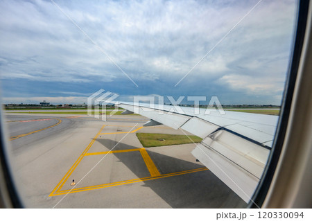 Through the airplane window, Suvarnabhumi International Airport comes into view, along with the expansive wings of the aircraft, amid the midday hustle. 120330094