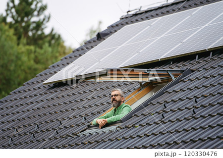 Man looking from skylight, roof window with solar panels above him. Sustainable lifestyle and green household. Man looking from skylight, roof window with solar panels above him. Sustainable lifestyle and green household. 120330476