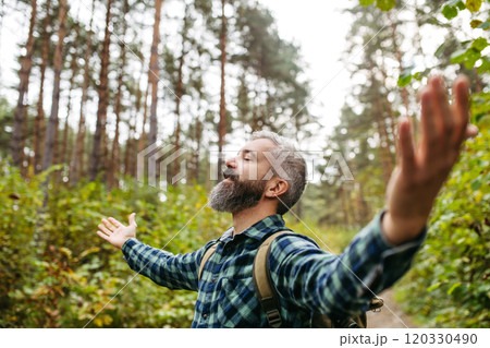 Handsome man standing in the middle of nature with open arms, enjoying peaceful atmosphere of the forest, forestbathing. 120330490