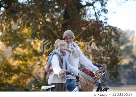 Elderly couple on walk in park, pushing their bikes side by side. Seniors in love on stroll through autumn city, enjoying a peaceful moment together. 120330517