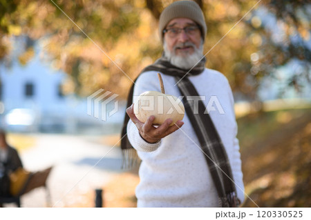 Portrait of smiling older man with pumpkin in hand. Senior standing outdoors in nature, looking at camera. 120330525