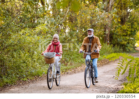 Beautiful elderly couple on bike ride in the forest. Seniors in love cycling through autumn nature, enjoying a peaceful moment. 120330554