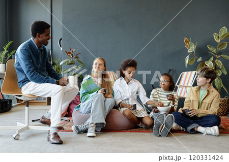 Full length shot of multiethnic group of children sitting on bean bags in creative studio and talking to teacher Full length shot of multiethnic group of children sitting on bean bags in creative studio and talking to teacher 120331424