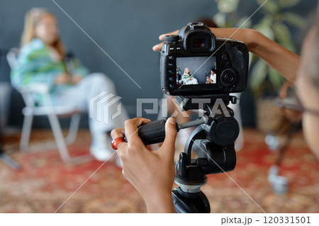 Close up of teenage kid setting up camera on tripod in studio and working with equipment settings at digital screen, copy space 120331501