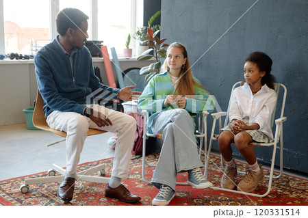 Full length portrait of adult African American man as male teacher or mentor helping two teen girls in studio and giving direction on creative project 120331514