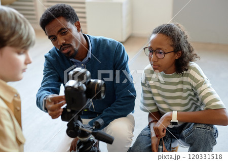 Portrait of African American man as male teacher helping children setting up video camera for creative project in art club 120331518