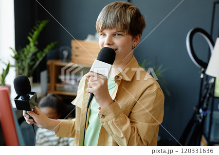 Waist up portrait of smiling teenage boy speaking to microphone while recording podcast with school club in studio Waist up portrait of smiling teenage boy speaking to microphone while recording podcast with school club in studio 120331636