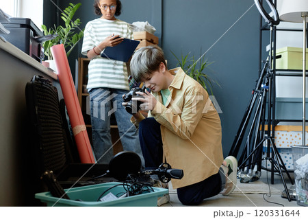 Side view portrait of young teenage boy setting up camera backstage and taking photos of equipment in studio, copy space 120331644