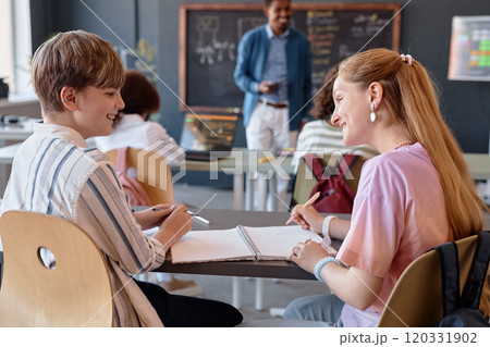 Side view portrait of smiling boy and girl chatting while studying together in school classroom and taking notes copy space Side view portrait of smiling boy and girl chatting while studying together in school classroom and taking notes copy space 120331902