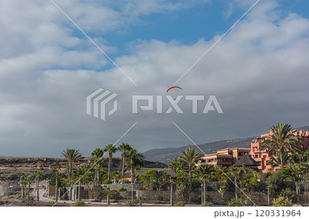 Paraglider soars over mountainous terrain and buildings. 120331964