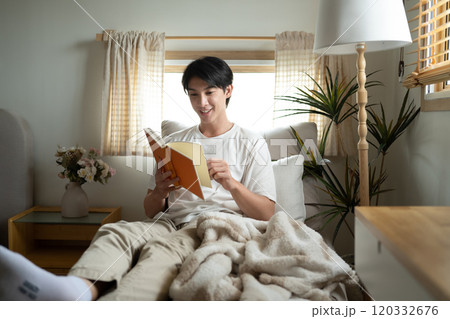 Handsome millennial man relaxing with a book in a living room Handsome millennial man relaxing with a book in a living room 120332676