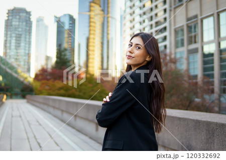 Confident businesswoman standing outdoors in a cityscape, looking back over her shoulder with subtle smile 120332692