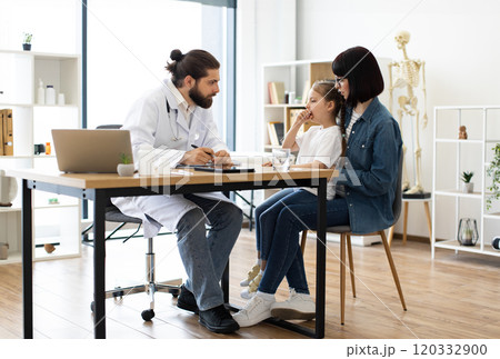 Caucasian doctor examining young girl with mother in clinic 120332900