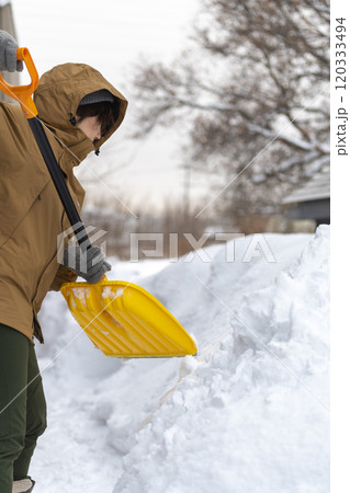 スコップで雪かきをする若い女性 120333494