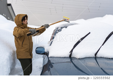 車に積もった雪を下ろす若い女性 120333502