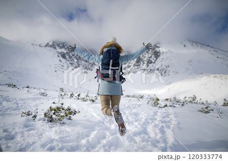 Woman jumping in the middle of the snowy nature with open arms, looking at the winter landscape around her. Woman jumping in the middle of the snowy nature with open arms, looking at the winter landscape around her. 120333774