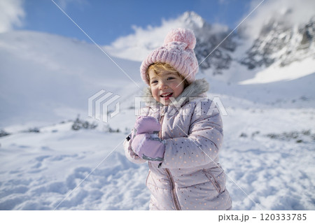 Portrait of small girl enjoying winter holiday in the mountains with family, playing in snow. 120333785