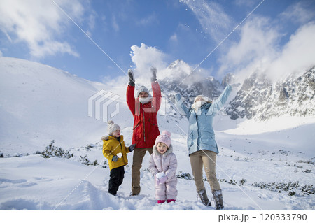 Young family is enjoying winter holiday in the mountains, standing in the middle of snowy landscape and throwing snow in the air . 120333790