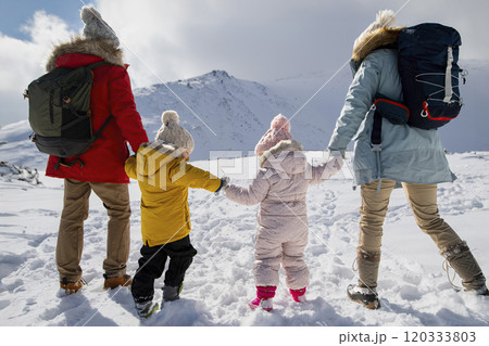 Young family is enjoying winter holiday in the mountains, holding hands while walking through the snowy landscape. Young family is enjoying winter holiday in the mountains, holding hands while walking through the snowy landscape. 120333803