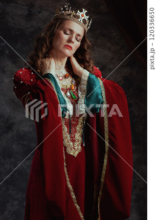 tired medieval queen in red dress with crown having neck pain 120336650