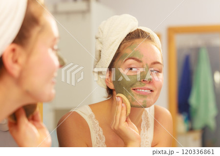 Woman removing facial clay mud mask in bathroom Woman removing facial clay mud mask in bathroom 120336861